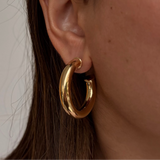 Gold hoop earring worn by a person with a neutral background