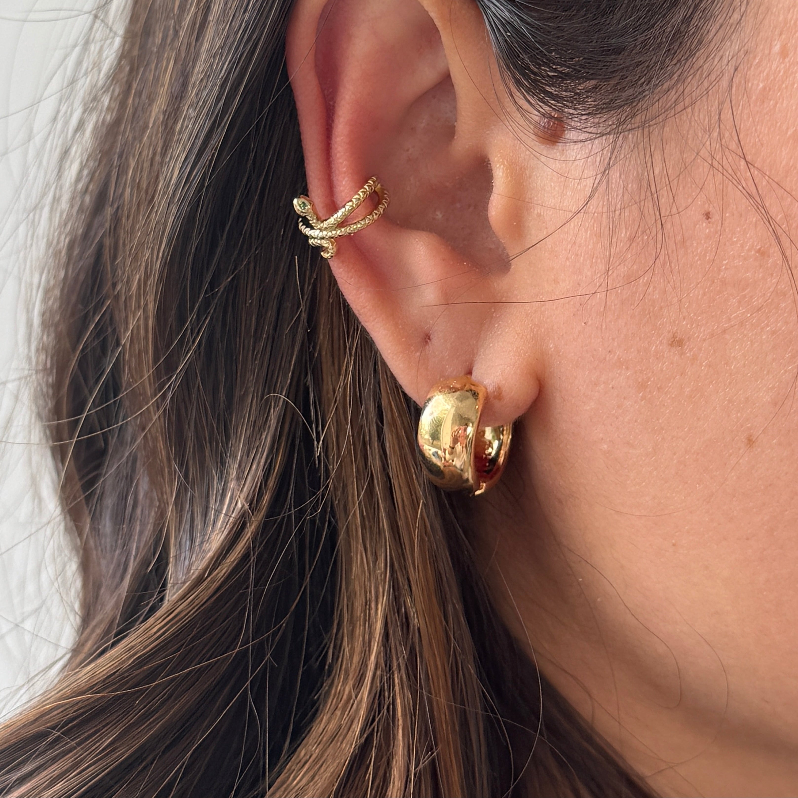 Close-up of an ear wearing gold hoop earrings with a neutral background