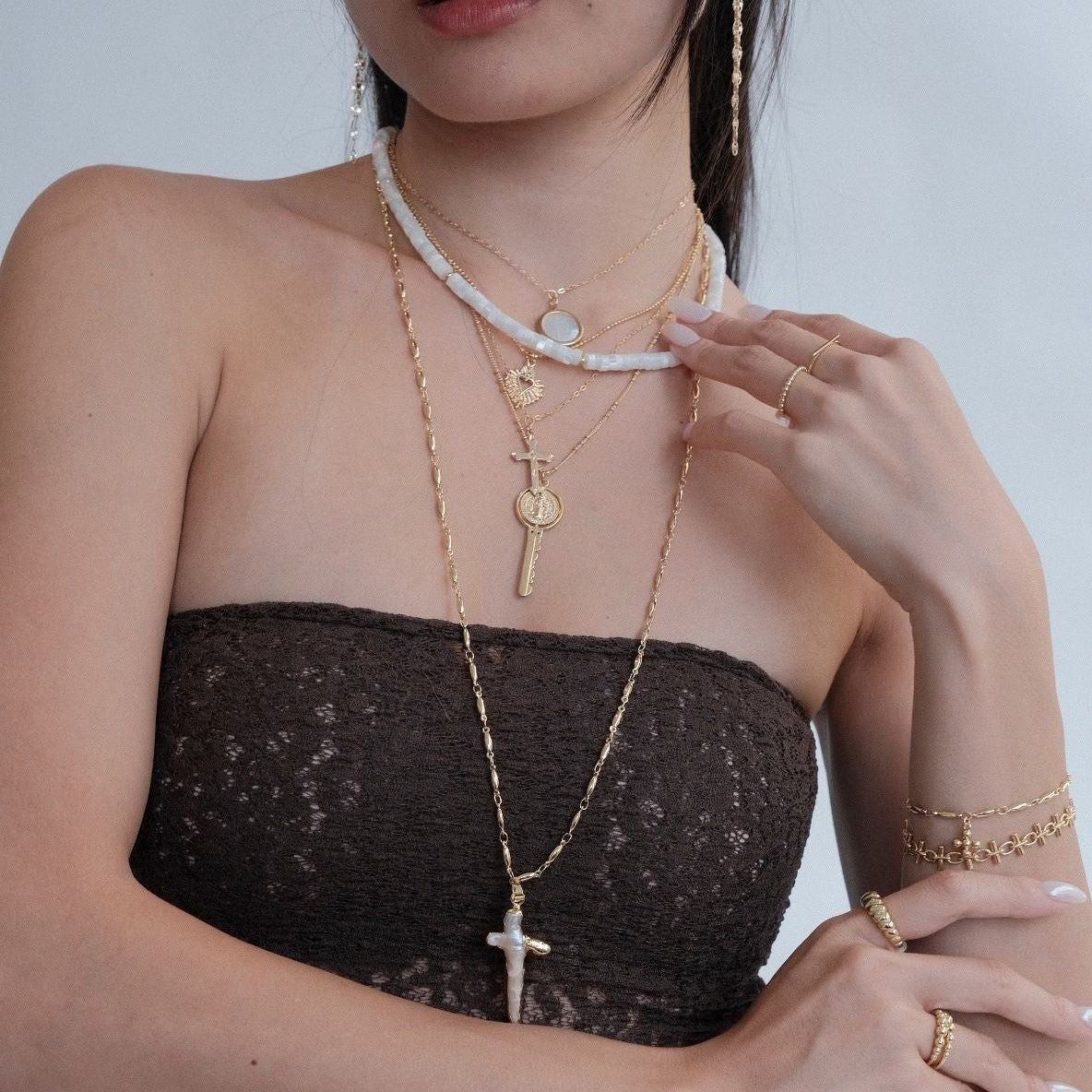 Woman wearing multiple necklaces and a bracelet against a plain background